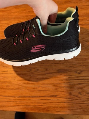 Svarta Skechers sneakers med memory foam - Svarta Skechers sneakers i textil med vit sula och rosa detaljer. Skorna har elastisk snörning, turkosfärgad insida och mjuk memory foam-innersula för extra komfort. Perfekta för dig som vill ha snygga och bekväma skor till vardagen. Inköps pris 899 