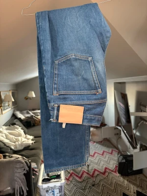 Blå jeans från Acne Studios - Säljer ett par klassiska blå jeans från Acne Studios med raka ben och stor bakficka. Jeansen har en ljus läderpatch bak och är gjorda i slitstarkt bomullsjeans. 