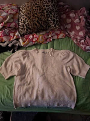 Beige stickad tröja med puffärm - Säljer en beige stickad tröja, med puffiga korta ärmar och ribbade muddar. Tröjan har en enkel, stilren design och är perfekt för lager på lager under höst och vår. Superskön och lätt att matcha med allt! Men har dock en liten fläck, en liten mascara fläck.