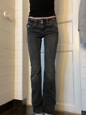Grå/svarta bootcut jeans från Gina Tricot - Säljer ett par svarta bootcut jeans från Gina Tricot med låg midja och dubbla knappar framtill. Jeansen har coola slitningar, kontrastsömmar och en liten ficka med lock och knapp. Storlek 158 skriv om du har frågor.