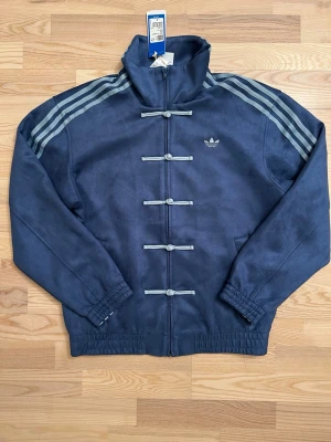 Adidas Originals CNY Chinese New Year Tang Jacka S NY - Den virala Adidasjackan säljes, köptes i Kina där denna kollektion säljs exklusivt. Mycket sällsynt fynd, helt ny och oanvänd, prislappen är kvar, Äkta vara. Stor i storleken. Oversized look.