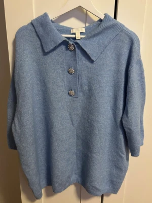 Ljusblå stickad pikétröja H&M L - Supersöt ljusblå stickad pikétröja från H&M i storlek L. Tröjan har en klassisk krage och tre glittriga knappar framtill som ger extra detalj. 