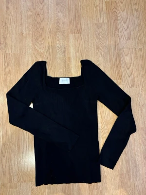 Svart ribbad topp från Neo Noir - Säljer en svart ribbad topp från Neo Noir i storlek 40. Toppen har lång ärm, fyrkantig ringning och är tillverkad i en mjuk blandning av viskos och nylon. Perfekt att styla med jeans eller kjol för en clean look.