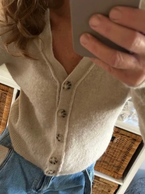 Beige kofta från Zara ull & alpacka Stl m  - Mysig beige kofta från Zara med v-ringning och fem snygga knappar framtill. Tröjan är i en mjuk mix av alpacka, ull och syntetmaterial, har lång ärm och ribbade muddar. Perfekt för lager på lager under kyliga dagar. Nypris 599;-