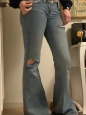 Cheap Monday ljusblå ripped jeans - Säljer ett par ljusblå jeans från Cheap Monday med slitna och trasiga detaljer på både lår och knä. Modellen har raka ben och klassisk femficksdesign. Jeansen är tillverkade i bomull och har en cool, vintage vibe med tydliga slitningar.