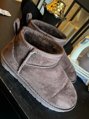 Bruna mockaboots med foder - Mysiga bruna boots i mocka med mjukt foder på insidan. Skorna har en låg profil, rund tå och platt sula. Perfekta för kyligare dagar och enkla att dra på tack vare öglor baktill.