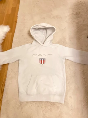 🤍 Vit GANT hoodie 🤍 -  Säljer en superfin vit hoodie från GANT i mycket bra skick. Perfekt för vinter, då den håller värmen bra och är både mjuk och bekväm. Passar jättebra för barn som vill vara stilrena men samtidigt hålla sig varma ❄️✨