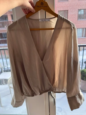 Topp/blus - En snygg topp/blus från NAKD. V-ringad med en liten knapp som håller den stängd. Snygga lite breda ärmar och en resår längst ner av toppen. Snygg färg, lite beige/guldig. Storlek 40🫶🏻