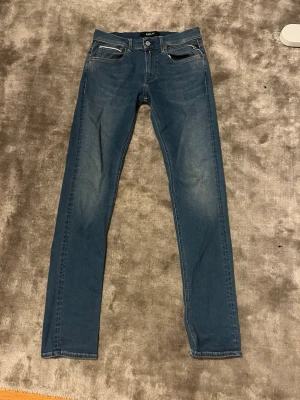 Blå Replay Hyperflex jeans straight fit - Säljer ett par blå Replay Hyperflex jeans med klassisk femficksdesign och raka ben. Jeansen har en snygg tvätt med lätt slitning på låren och är tillverkade i stretchigt jeansmaterial för extra komfort. Perfekta för dig som gillar en stilren och enkel look.