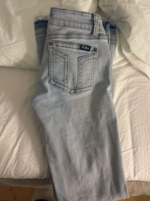 Ljusblå bootcut jeans från G.Rise - Säljer ett par ljusblå jeans från G.Rise med bootcut-modell och råa, fransiga benslut. Klassisk femficksdesign, normal passform och snygga detaljer med nitar vid fickorna. Perfekta för dig som gillar en avslappnad men trendig look.
