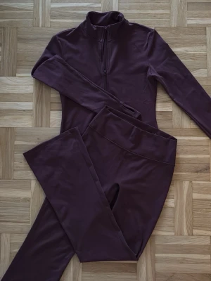 Träningsset i vinröd/lila – topp & tights - Snyggt och bekvämt träningsset i vinröd/lila ton. Setet består av långärmad topp med dragkedja samt matchande tights. Mjukt och följsamt material som passar både träning och vardag. Använt fåtal gånger, i mycket fint skick utan fläckar eller skador.