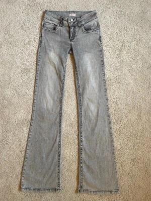 Grå bootcut jeans från Nelly - Säljer ett par grå bootcut jeans från Nelly med snygg tvätt och svarta kontrastsömmar. Jeansen har dubbla knappar och klassiska fickor med zigzag-detalj bak. De är sparsamt använda pga att de var för stora när jag köpte dem. Däremot är det lite sönder på kanten nere på ena benet (de sista bilden).💓