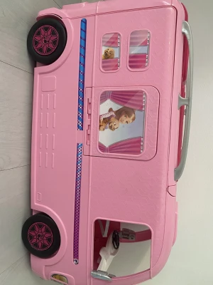 Barbie husbil - Säljer en fin Barbie husbil/campingbil i rosa färger med många roliga detaljer. Husbilen kan öppnas upp och innehåller flera rum, bland annat kök, badrum med dusch och sov-/lekyta. Perfekt för fantasifull lek! Allt som syns på sista bilden ingår gratis! Allt är i fint skickt som det syns på bilden. 