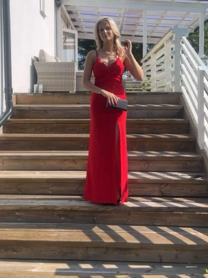 Röd långklänning med spets och slits - Säljer min balklänning , det är en röd långklänning med smala axelband, v-ringning och spetsdetaljer upptill. Klänningen har en snygg slits framtill och figurnära passform. Perfekt för bal eller student! Materialet känns mjukt och följsamt.