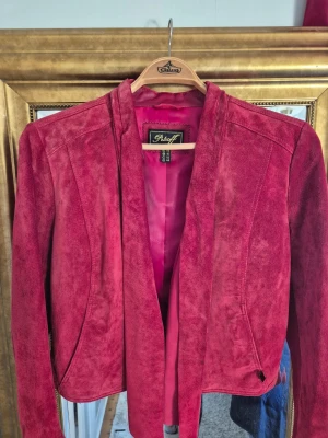 Röd mockajacka från Petroff - Säljer en snygg röd mockajacka från Petroff med öppen front och mjukt material. Jackan har en stilren design utan krage och är helfärgad i en djup röd ton. Perfekt för dig som vill ha en unik och trendig jacka med skön passform.