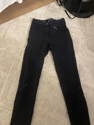 Mörkblåa  ridbyxor från CRW, strl 38 - Säljer ett par mörkblåa ridbyxor från CRW i storlek 38. Byxorna har helskoning med silikonprickar för extra grepp och en smal passform. Klassisk look med knapp och dragkedja framtill. Perfekta för dig som vill ha stilrena och funktionella ridbyxor.