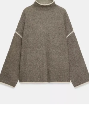 Beige stickad tröja med vida ärmar - Säljer en beige stickad tröja med hög hals och vida, långärmade ärmar. Tröjan har diskreta vita detaljer vid hals, ärmslut och nederkant. Perfekt för lager-på-lager och chill höst- och vinterstil.