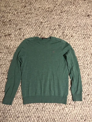 Grön merinoullströja från Morris - Snygg grön rundhalsad tröja från Morris i mjuk merinoull. Diskret Morris-logga broderad på bröstet. Tröjan har lång ärm och ribbade muddar vid ärmslut och nederkant. Perfekt för dig som gillar stilrena och bekväma plagg.