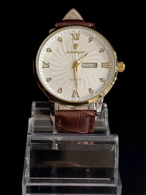 Poedagar Imperial Leather – Diamond Roman - Poedagar Imperial Leather – Diamond Roman är en elegant och tidlös armbandsklocka som kombinerar klassisk romersk design med moderna lyxdetaljer. Den ljusa, strukturerade urtavlan pryds av romerska siffror och diamantliknande markeringar som ger ett exklusivt uttryck. Det bruna läderarmbandet ger en sofistikerad kontrast till boetten i guldfinish och gör klockan perfekt för både vardag och mer formella tillfällen. Quartz-urverk med datum- och dagsvisning. Levereras i originalbox. Helt ny.