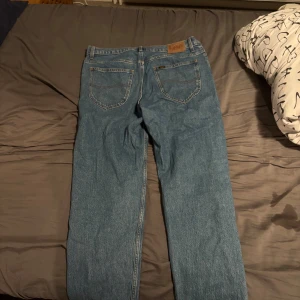 Blå Lee jeans Oscar W34 L32 - Klassiska blå jeans från Lee, modell Oscar. Jeansen har rak passform, fem fickor och snygga kontrastsömmar. Tillverkade i slitstarkt bomullsjeansmaterial, perfekta för en avslappnad och tidlös look. Har använts några fåtal gånger. Priset är diskuterbart!