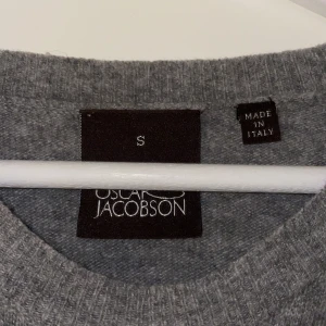 Grå stickad tröja från Oscar Jacobson 100% Kashmir  - Säljer en stilren grå stickad tröja från Oscar Jacobson med broderad OJ-logga på ärmen. Tröjan har rund halsringning och långa ärmar, perfekt för lager-på-lager. Tillverkad i Italien och känns både mjuk och lyxig. Topp skick utan några defekter, hör av er vid frågor !