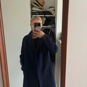 Mörkblå kappa H&M   - Säljer en stilren mörkblå kappa i ullmix med skärp i midjan och klassisk krage. De är storlek 40 men är liten i storleken!