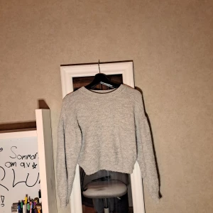 Grå croppad stickad tröja - Barn. Storlek 146/152. Mysig grå stickad tröja med croppad passform och rund hals. Tröjan har långa ärmar och en enkel, stilren look som passar perfekt till jeans eller kjol. Ribbad struktur ger extra detalj och komfort.