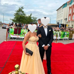 Gul/Champagnefärgad lång balklänning - Säljer denna fina balklänning i gult/champgane✨. Den är axelbands lös och har en vacker spetsdesign på överdelen samt en lång flödande kjol (litet släp). Perfekt för bal eller fest❣️. Som bilderna visar har klänningen inte kemtvättats, så det kan behövas eller eventuellt sy upp om man skulle vilja det.