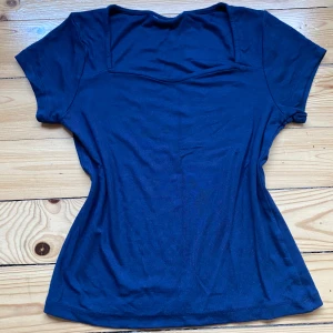 Mörkblå topp med fyrkantig ringning - En enkel och stilren mörkblå topp med korta ärmar och fyrkantig ringning. Toppen har en figurnära passform och är tillverkad i ett mjukt bomullsmaterial som känns skönt mot huden. Perfekt att matcha med jeans eller kjol för en avslappnad look. Finns ingen lapp men skulle tro att den är i storlek 158 den passar som en XS. 