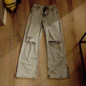 Ljusblå wide leg jeans med slits - Ljusblå jeans från &Denim i wide leg-modell med hög midja. Byxorna har slitna hål på båda knäna och slitsar nertill vid bensluten. Tillverkade i klassisk denim, perfekta för en avslappnad och trendig look.