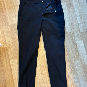 Svarta kostymbyxor från Zara Woman S - Snygga svarta kostymbyxor från Zara Woman i storlek S. Klassisk rak modell med hällor för bälte, snedställda fickor fram och passpoalfickor bak. Perfekta för en clean och stilren look. Materialet känns mjukt och följsamt.