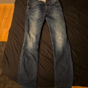 Jacob Cohën blå jeans bootcut - Snygga blå jeans från Jacob Cohën med bootcut passform och klassisk femficksdesign. Jeansen har tydliga slitningar framtill, röda sömmar och knäppning med knappar. Tillverkade i exklusivt denimtyg med italianskt hantverk. Perfekta för dig som gillar stilrena jeans med unik touch.