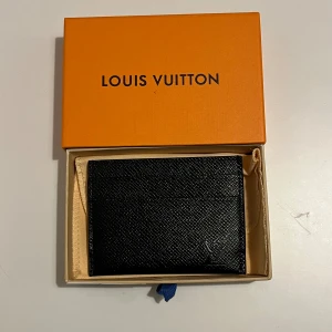 Svart korthållare med diskret logga - Säljer en stilren svart plånbok i exklusivt skinn med diskret struktur. Kommer i original ask och dustbag. Perfekt för kort och sedlar, smidig att ha med sig i fickan eller väskan.