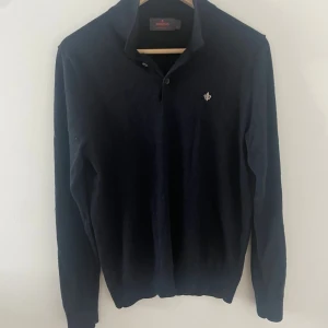 Mörkblå merinoull polotröja Morris - Snygg mörkblå polotröja från Morris i 100% merinoull. Tröjan har klassisk krage med knappar och en liten broderad logga på bröstet. Perfekt för dig som gillar stilrena och bekväma plagg med premiumkänsla.