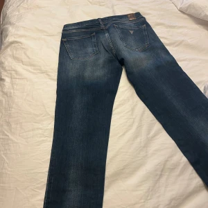 Guess skinny jeans med slitningar - Säljer ett par blå skinny jeans från Guess med rejält slitna detaljer framtill. Jeansen har klassisk femficksdesign, normalhög midja och är tillverkade i jeansmaterial. Perfekta för dig som gillar en edgy och trendig look.