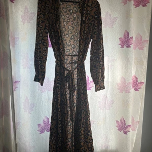 Långklänning med leopardmönster och knyt - Säljer en långklänning med snyggt leopardmönster i bruna och svarta toner. Klänningen har långa ärmar och ett knytband i midjan som ger en schysst siluett. Perfekt för dig som vill sticka ut lite extra med ett djurmönster.