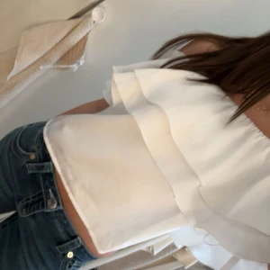Vit offshoulder volangtopp - Säljer en superfin vit offshoulder topp med dubbla volanger. Toppen är ärmlös och har en luftig, flowy känsla. Perfekt till jeans eller kjol för en fräsch look. Materialet känns lätt och svalt. Går att bära med one shoulder också!❣️aldrig använd 