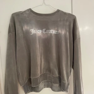Grå velourtröja från Juicy Couture - Supermjuk grå velourtröja från Juicy Couture med silvrigt logotryck på bröstet. Tröjan har avslappnad passform, rund hals och långa ärmar. Perfekt för dig som gillar en chill och trendig stil. Endast använd förtal gånger.