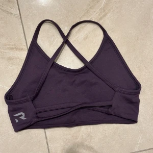 Mörklila linnetopp med korsade band - Säljer en mörklila linnetopp från stadium med smala korsade axelband i ryggen. Toppen är enkel och stilren med en liten logga på sidan. Perfekt för träning eller chill dagar. Materialet är mjukt och stretchigt för bästa komfort. Köpt för 500 från stadium 