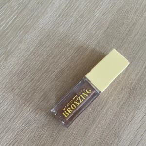 Makeup Mekka Bronzing - Flytande bronzer från Makeup Mekka i en snygg brun nyans. Kommer i en genomskinlig fyrkantig flaska med gul kork och text i guld. Perfekt för att ge ansiktet en solkysst look.
