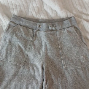 Grå mjukisbyxor från Juicy Couture - Säljer ett par grå mjuka byxor från Juicy Couture med bred resår och snörning i midjan. De har två stora fickor fram och en liten broderad JC-logga på ena sidan. Tillverkade i bomullsmix för extra komfort. Dock så har byxorna en liten fläck, som inte syns alls mycket(det fins bild på fläcken) Och där framme så har en av silver tillbehören åkt bort I tvätten(fins även bild på det)! Men jag tycker verkligen att dom är så sköna nu till vintern och hösten,jag är öppen med att byta pris på dom💕🫶🏻