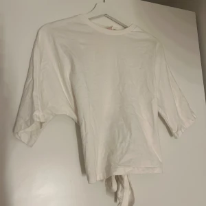 Vit croppad topp med knyt i ryggen - Säljer en vit croppad topp med korta ärmar och snygg knytning i ryggen. Toppen har en enkel och clean look med rund hals och är gjord i mjuk bomull. Perfekt för dig som gillar stilrena plagg med en twist på ryggen.