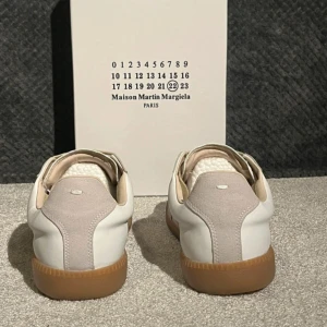 Maison Margiela  - Maison Margiela sneakers i en clean beige och vit färgkombination med klassisk gummisula. Ovandelen är i skinn och mocka, med beige snörning och rund tå. Snygg minimalistisk design som passar till allt och ger en lyxig vibe.