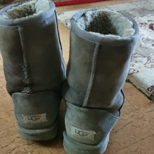 Grå UGG boots i mocka - Mysiga grå boots från UGG med mjukt foder och klassisk rund tå. Skorna är i mocka och har en platt sula, perfekta för kalla dagar. UGG-logga baktill och högt skaft som värmer ordentligt.