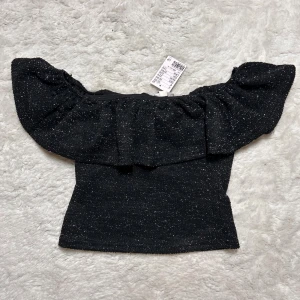 Off shoulder volang top glittrig  - Glitter topp från h&m. Köpt för ungefär ett år sedan. Helt ny med prislapp. I storlek xs men passar även en s.  Köp sker via köp nu, jag postar inom 24h. Kvar tills markerad såld