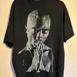 Svart 2Pac t-shirt loose fit M - Svart t-shirt med stort tryck av Tupac Shakur på framsidan och ikoniskt citat på ryggen. Oversized loose fit, rund hals och korta ärmar. Grym streetstyle med tydlig hiphop-vibe. Materialet är mjuk bomull.