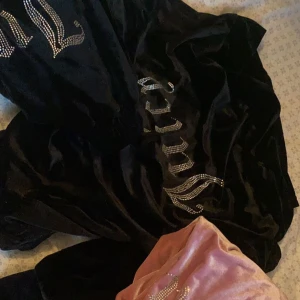 Svart juicyhoodie med strass - Cool svart hoodie i mjuk sammet med stora glittriga strassdetaljer på bröstet. Perfekt statement-plagg för dig som gillar att sticka ut. Oversized fit och med huva för extra comfy känsla.