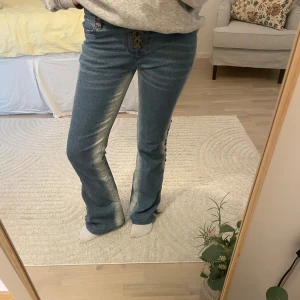 Blå bootcut jeans med snörning - Unika ljusblå bootcut jeans från 5PM med cool snörning framtill och längs sidorna. Jeansen har låg midja. Perfekta för dig som vill sticka ut med en unik detalj på dina jeans.