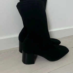 Svarta mocka stövletter med klack - Snygga svarta stövletter i mocka med spetsig tå och stabil klack. De har en stilren och smal siluett som ger en cool vibe till din outfit. Perfekt för dig som gillar minimalistisk stil och vill ha boots som sticker ut lite extra.