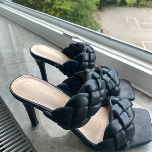 Svarta flätade klack-sandaler - Snygga svarta sandaler med hög klack från Viva Couture. Skorna har två breda, flätade remmar över foten och fyrkantig tå. Tillverkade i syntetmaterial med en stilren och modern look. Perfekta för dig som vill sticka ut med trendiga detaljer.Från newyorker